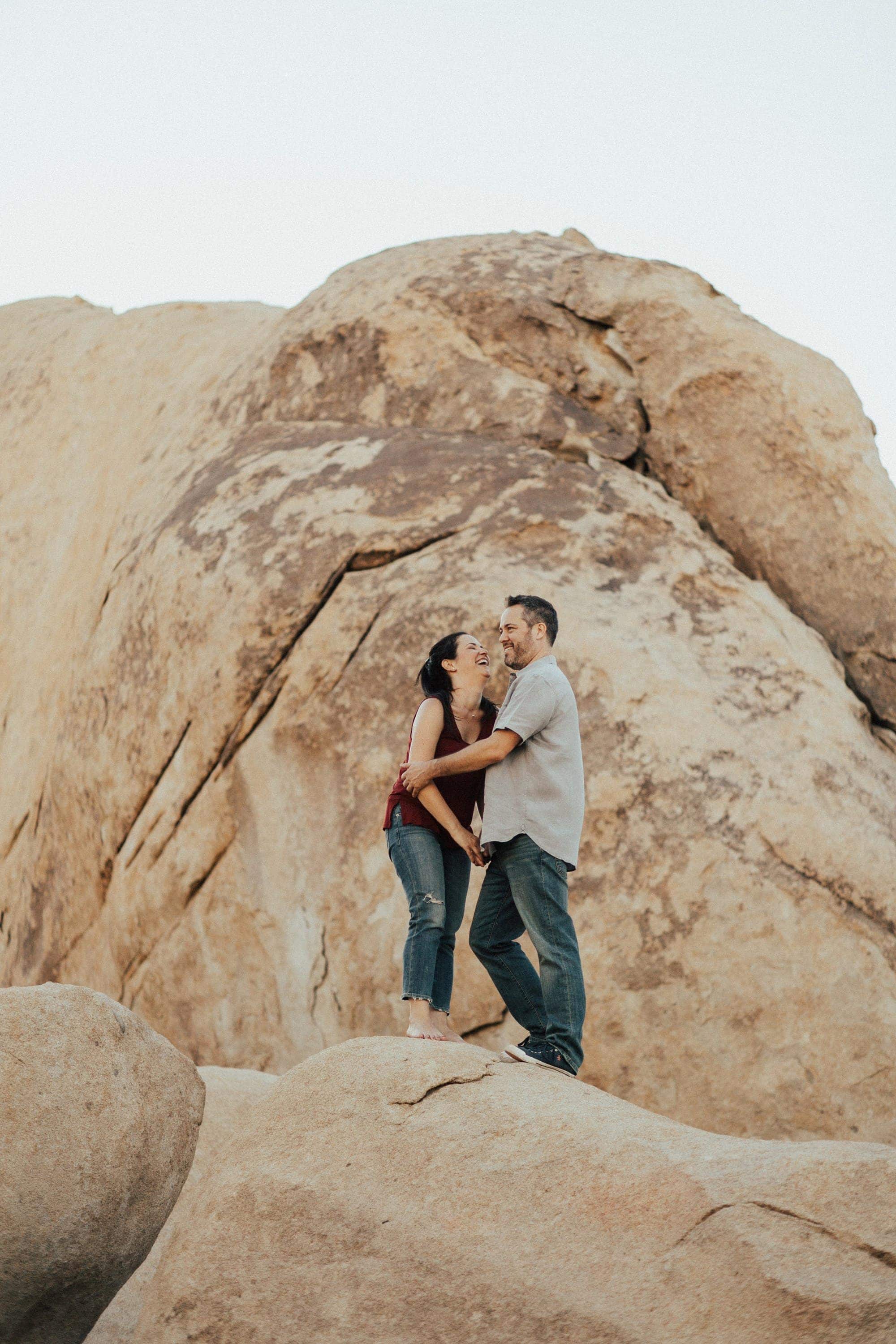 sweet engagement photo of a couple standing on boulders in joshua tree national park