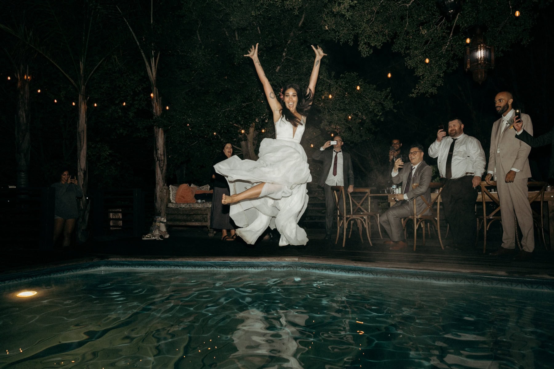 bride jumping in pool with wedding dress