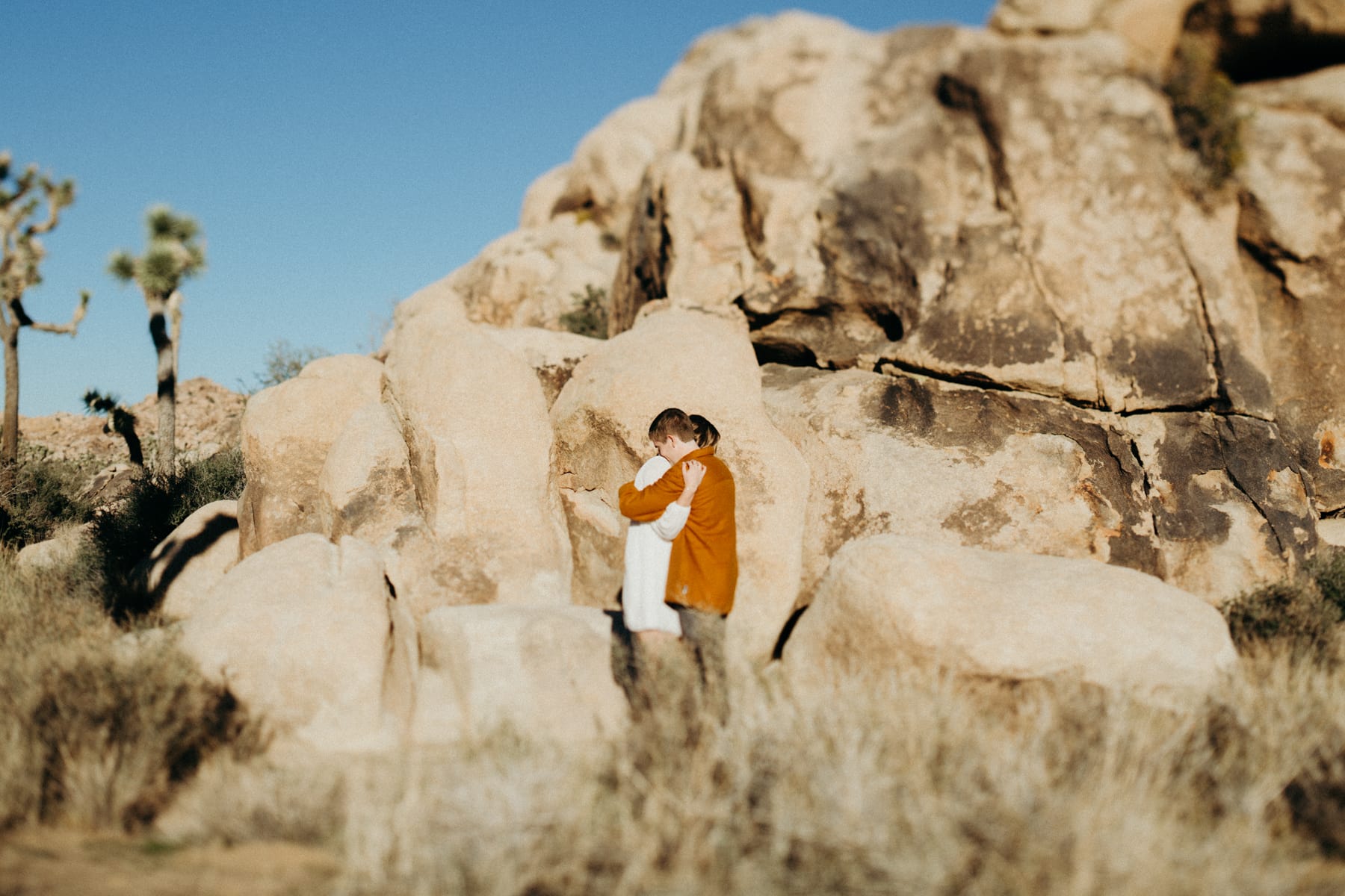 guy and girl hugging in front of a boulder in joshua tree