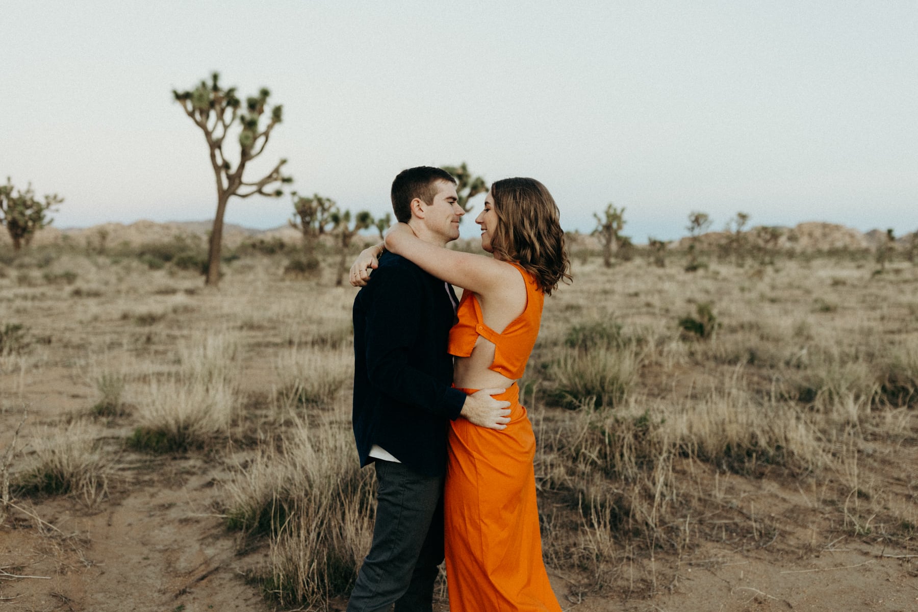 couple snuggling in the desert with the woman wearing a bright orange outfit