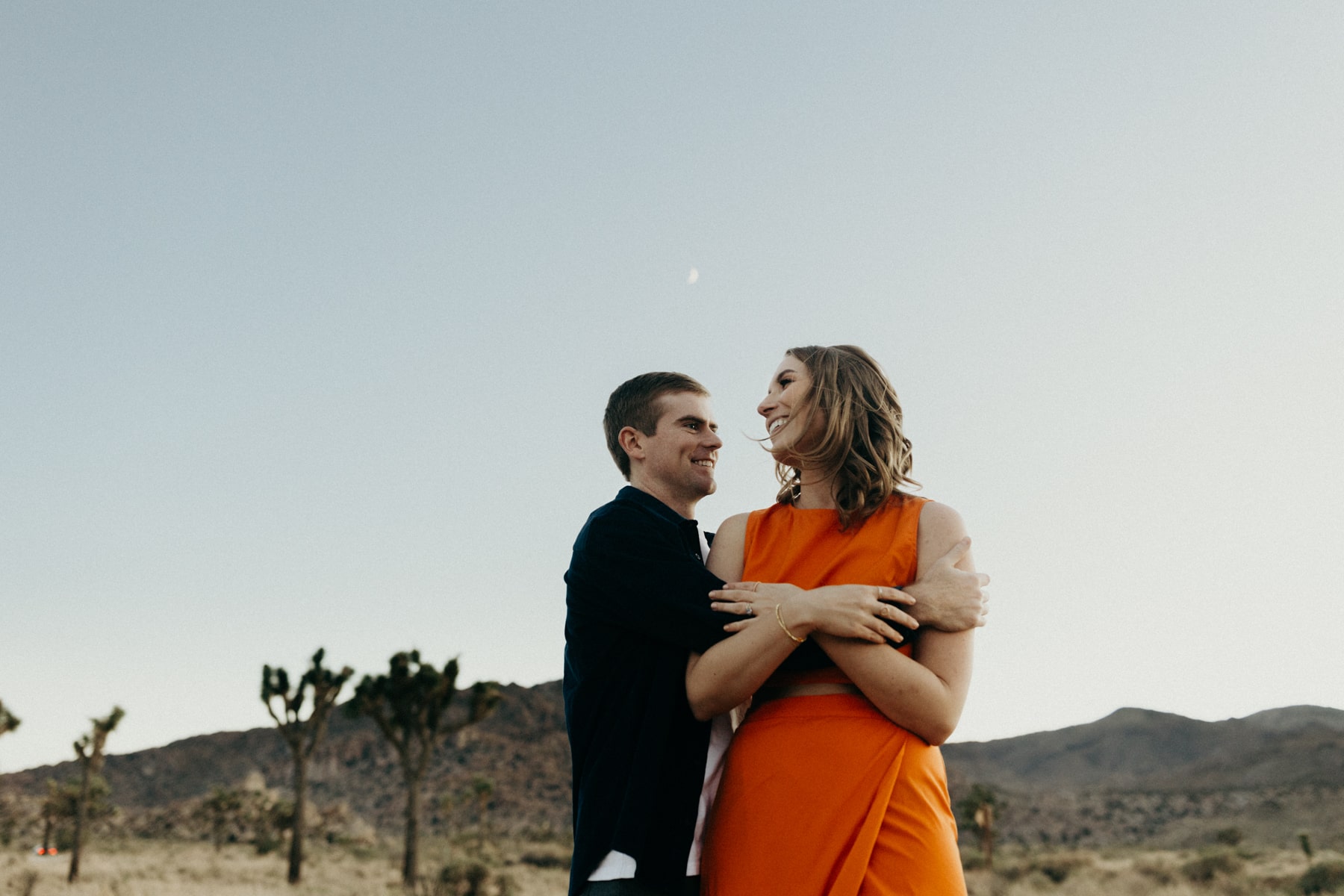photo of a couple in the desert with the moon high above them