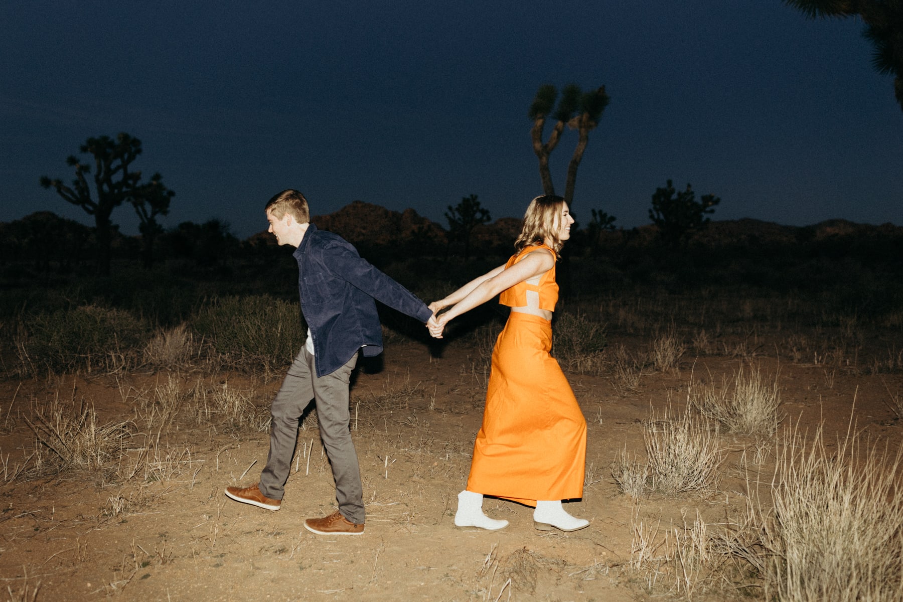 couple holding hands goofing off in the desert with flash photography