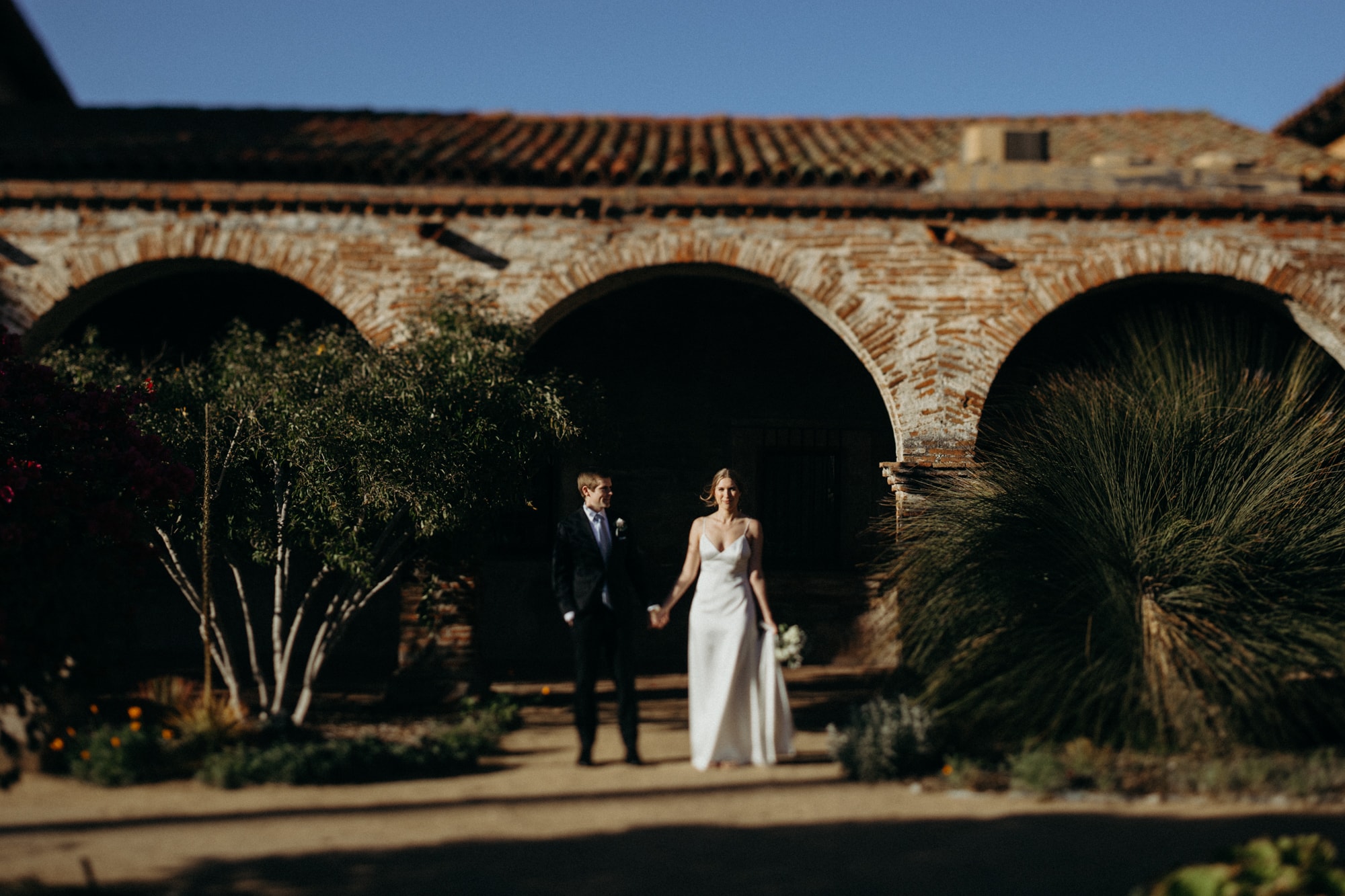 couple holding hands standing in front of mission san juan capistrano